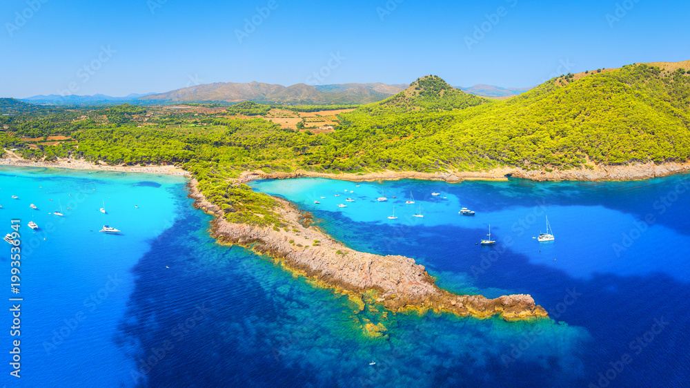 Fototapeta premium Aerial view of Cala Agulla beach and turquoise bay with boats in Mallorca. Scenic Balearic Islands coastline landscape in Spain. Summer vacation and Mediterranean nature from drone.