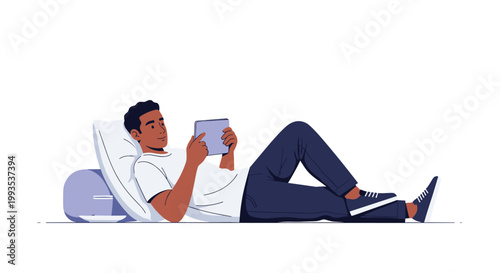 Young man lies comfortably on a large white pillow while using a digital tablet for entertainment or work at home.
