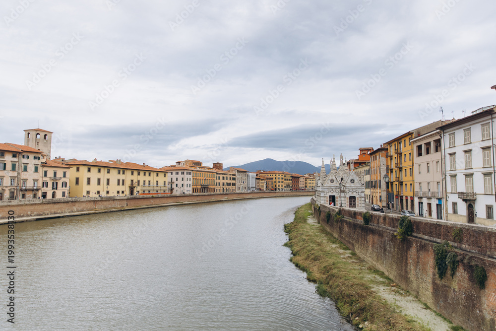 Fototapeta premium Arno river flowing through Pisa cityscape with Santa Maria della Spina and historic buildings in Tuscany, Italy