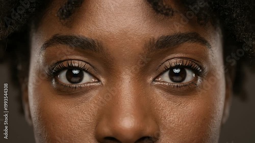 Close-up portrait of a young woman with natural curls, showcasing her expressive eyes against a neutral background