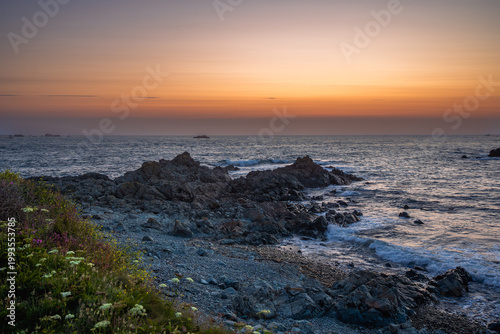 Vibrant sunset over the Atlantic Ocean near Guernsey, Channel Islands, with deep orange and red sky reflecting on calm water.