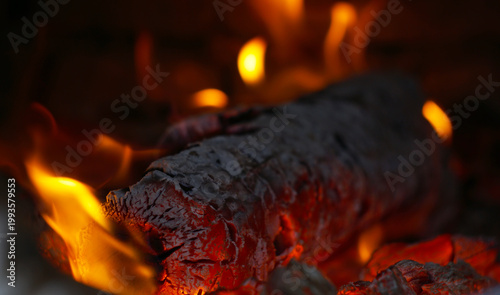 Close-up of a burning log with red hot embers and orange flames.