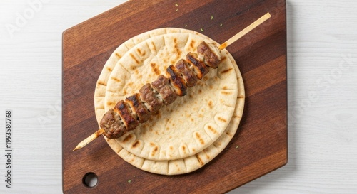Skewered grilled meat on flatbread, wooden board, white background