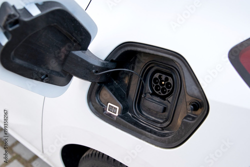 Electric vehicle charging port with connector attached, showcasing the charging mechanism and design details on a white car parked on a paved surface