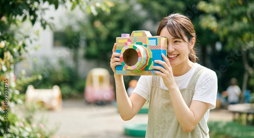 手作りカメラで遊ぶ保育士の女性 園庭 工作 幼稚園 笑顔