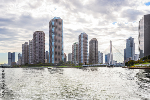 Riverbank development with tall apartment towers on a cloudy autumn day. A modern suspension bridge connects the development to the the other bank of the river. Tokyo, Japan.