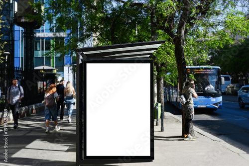 blank lightbox and glass bus shelter at bus stop. soft urban street background. white ad poster. display panel. empty outdoor ad space. mockup base. blue bus and passenger on the sidewalk