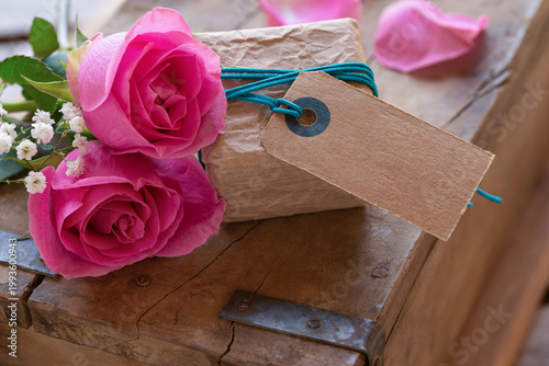 Cute little gift package with cardboard label, space for text and pink roses on old wood – Mother's Day – Birthday