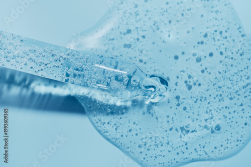 Clear liquid serum with bubbles flowing from dropper on blue background