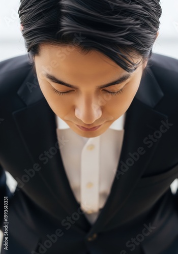 Japanese Businessman In Suit Bowing Respectfully Looking Down With Eyes Closed In Professional Office Setting