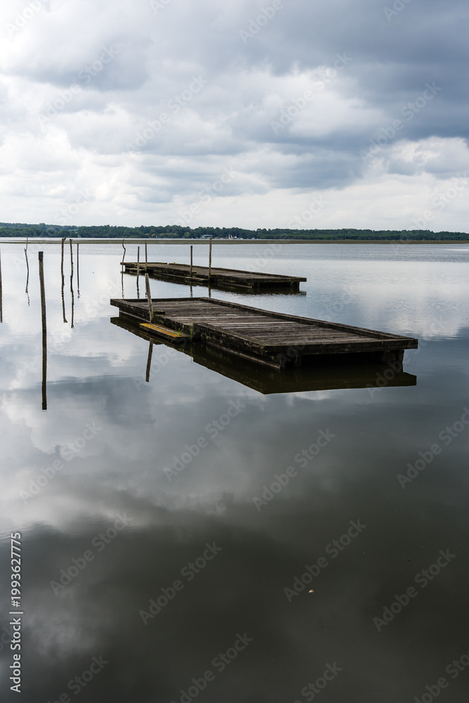 Fototapeta premium Lake of Soustons reflecting a cloudy sky and wooden docks