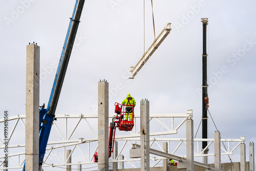 Bild auf Leinwand Worker in lift guides suspended steel beam as cranes position structure on concr