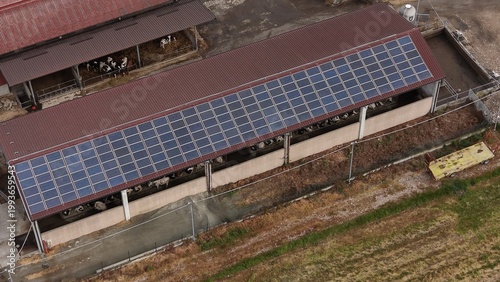 Farm Rooftop Solar Power: An aerial view of a farm building with a dark brown roof covered in solar panels, showcasing sustainable energy integration in an agricultural setting.