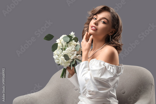 Beautiful bride with flowers sitting in armchair on dark background