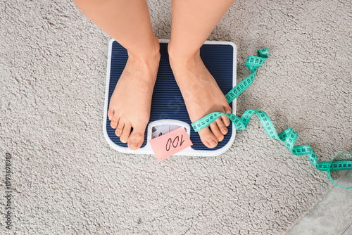 Bild auf Leinwand Woman's feet with tape measure and large number on weight scales at home, top view