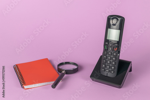Vintage Cordless Phone on Desk with Red Notebook and Magnifying Glass on Purple Background