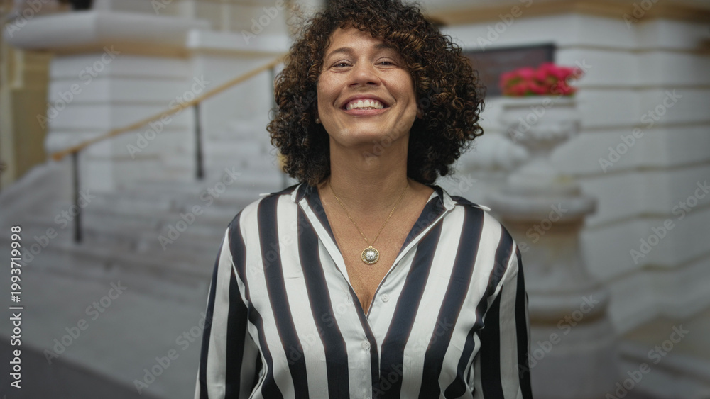 Fototapeta premium Woman in striped shirt wearing gold pendant smiling with finger pointing to head on street; idea happiness.