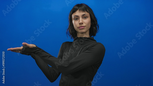 Obraz na plátně Young hispanic woman wearing tight black sports jacket holds palms up in studio demonstration; confidence