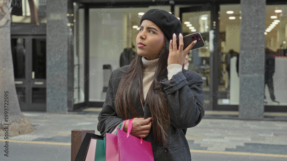 Obraz premium Young latin woman holding smartphone to ear with hand and clutching pink shopping bags outside a retail store on a busy street; frustration waiting.