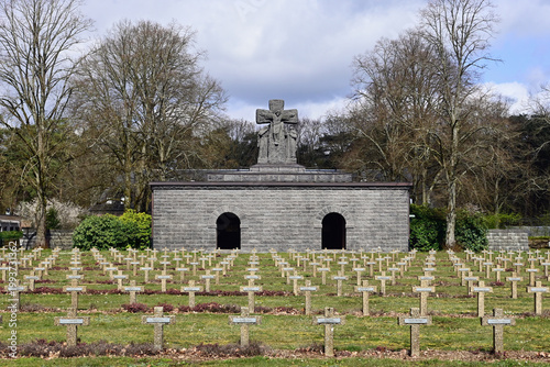 German WWII War Cemetery (at Lommel - Belgium) with a stone statue in a cemetery with rows of tombstones under a cloudy sky