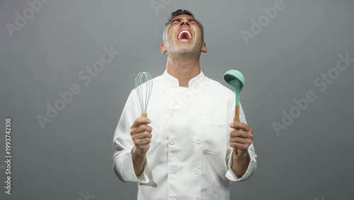 Fotografia Man chef holding whisk and ladle, mouth open and head tilted back in a studio; playful exuberance joy