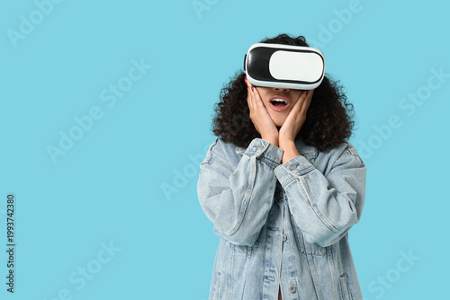 Surprised African-American woman with VR glasses on blue background
