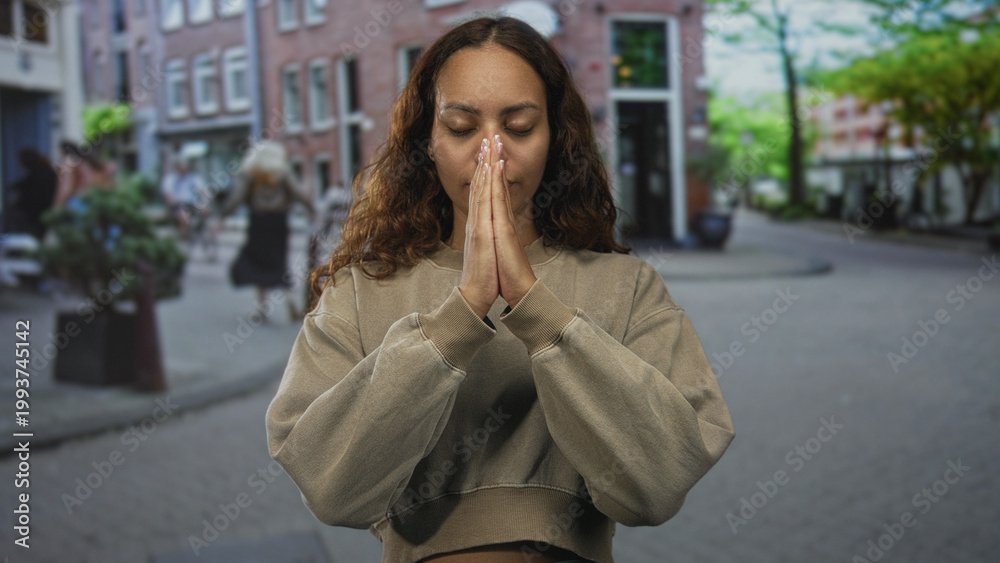 Fototapeta premium Woman with hands pressed together in prayer on a cobblestone street, cropped sweatshirt visible; serenity reflection.