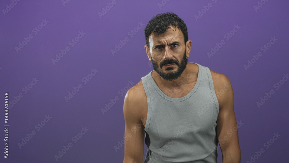 Obraz premium Man with beard frowning, bare arm visible while standing in studio against purple backdrop, leaning slightly and gazing forward; concern introspection.