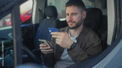 Fotografija Man in car holding creditcard and smartphone, hands tapping phone while seated on street; focused mobile payment