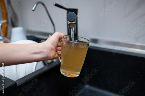 Hand Filling Glass Mug with Dirty Rusty Water from Kitchen Faucet Concept of Poor Water Quality