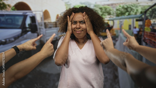 Cuadro en lienzo Woman holding forehead as several hands point fingers at her on a construction street; anxiety blame isolation