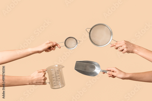 Canvastavla Female hands holding sieves with measuring cup and scoop on beige background