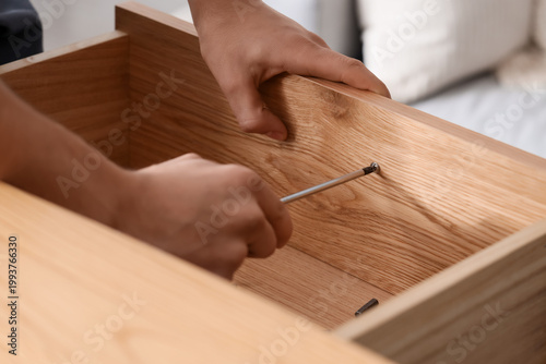 Obraz na plátně Male carpenter tightening screw in wooden drawer with screwdriver, closeup