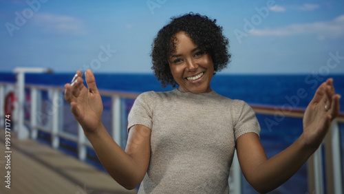 Obraz na plátne Woman extends arms on cruise deck with warm smile and curly hair against ocean backdrop; welcome happiness joy warmth