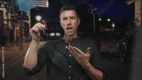 Quadro em tela Man young caucasian holds car key fob with raised hand and points to keys on street at night with open mouth; surprise lost item