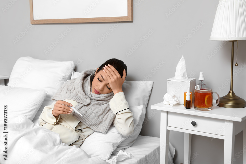 Fototapeta premium Ill young woman with thermometer lying in bedroom