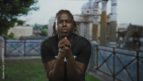 Fotografie Man wearing staff t shirt with hands clasped in prayer on building balcony outdoors; hope faith reflection
