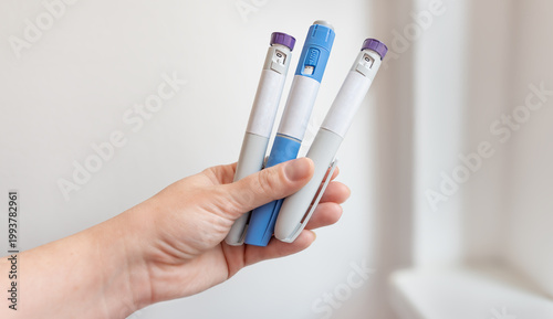 Hand holding multiple GLP-1 injection pens, modern diabetes and weight loss medication concept