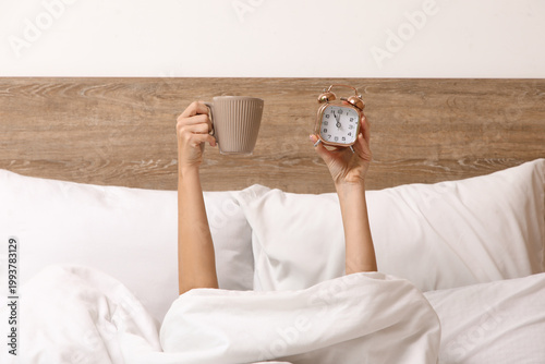 Konstfotografi Female hands with alarm clock and cup of coffee in bed at home