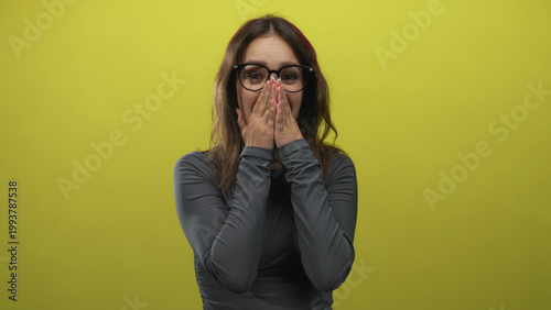 Photography Hispanic woman wearing glasses covering mouth in lime green studio while smiling and laughing; surprise candid moment
