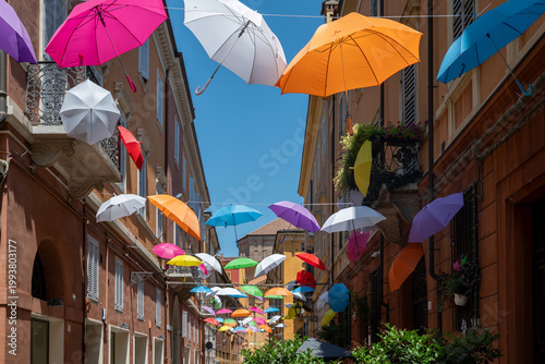 City street in Modena, Italy with rainbow colored umbrellas overhead, vibrant urban scene, summer atmosphere, travel destination