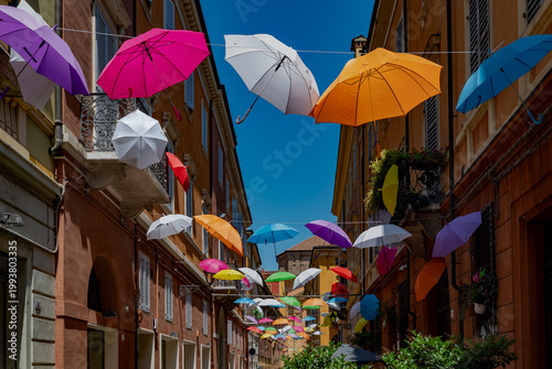 City street in Modena, Italy with rainbow colored umbrellas overhead, vibrant urban scene, summer atmosphere, travel destination