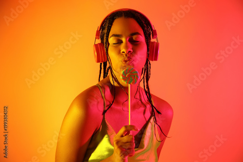 Young African-American woman with lollipop listening to music on color backgr...