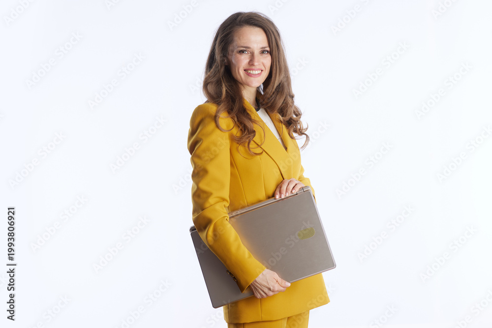 Obraz premium A smiling businesswoman in a yellow suit confidently holds a closed laptop at her side, symbolizing readiness for modern work and professional mobility.