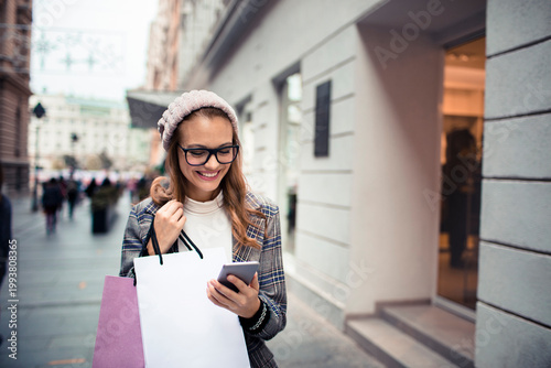 Smiling woman with shopping bags using smartphone on city street