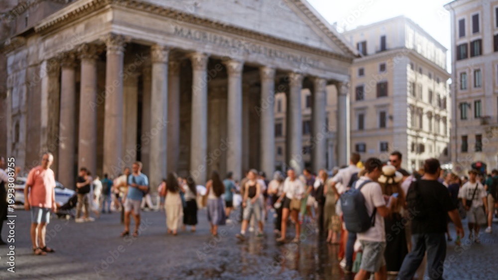 Obraz premium Shallow bokeh of a busy city plaza with defocused classical columns and sunlit cobblestone foreground; background backdrop copyspace calm.