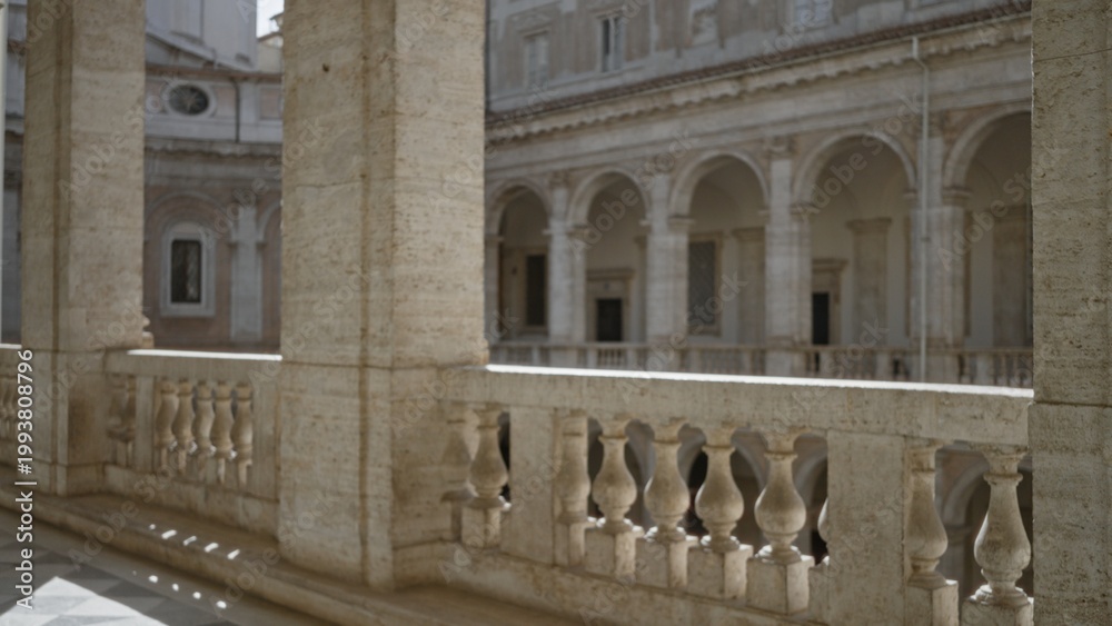 Fototapeta premium Weathered limestone balustrade and fluted columns overlooking a sunlit arched courtyard in soft blurred focus museum; background backplate copyspace calm.