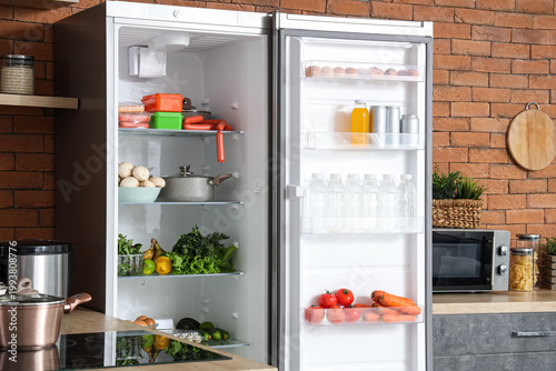 Slika na platnu Big modern fridge with fresh products on brown brick background in kitchen