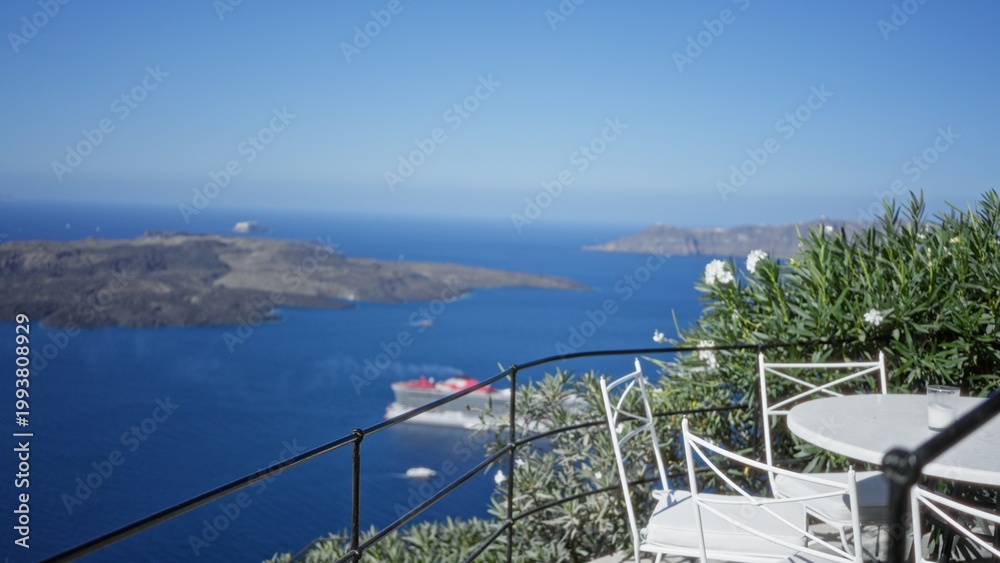 Fototapeta premium Terrace with white cafe chairs and metal railing in shallow blurred focus overlooking blue sea and distant islands outdoor; background copyspace.