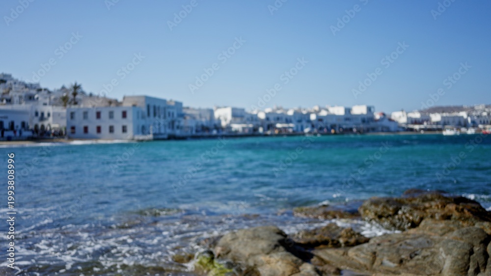 Fototapeta premium Coastal waterfront scene softly defocused bokeh background outdoor showing turquoise sea, blurred white buildings and rocky shore in shallow focus; background copyspace calm.